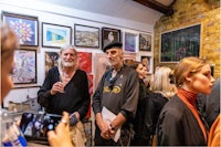 a group of people standing in front of a wall full of paintings